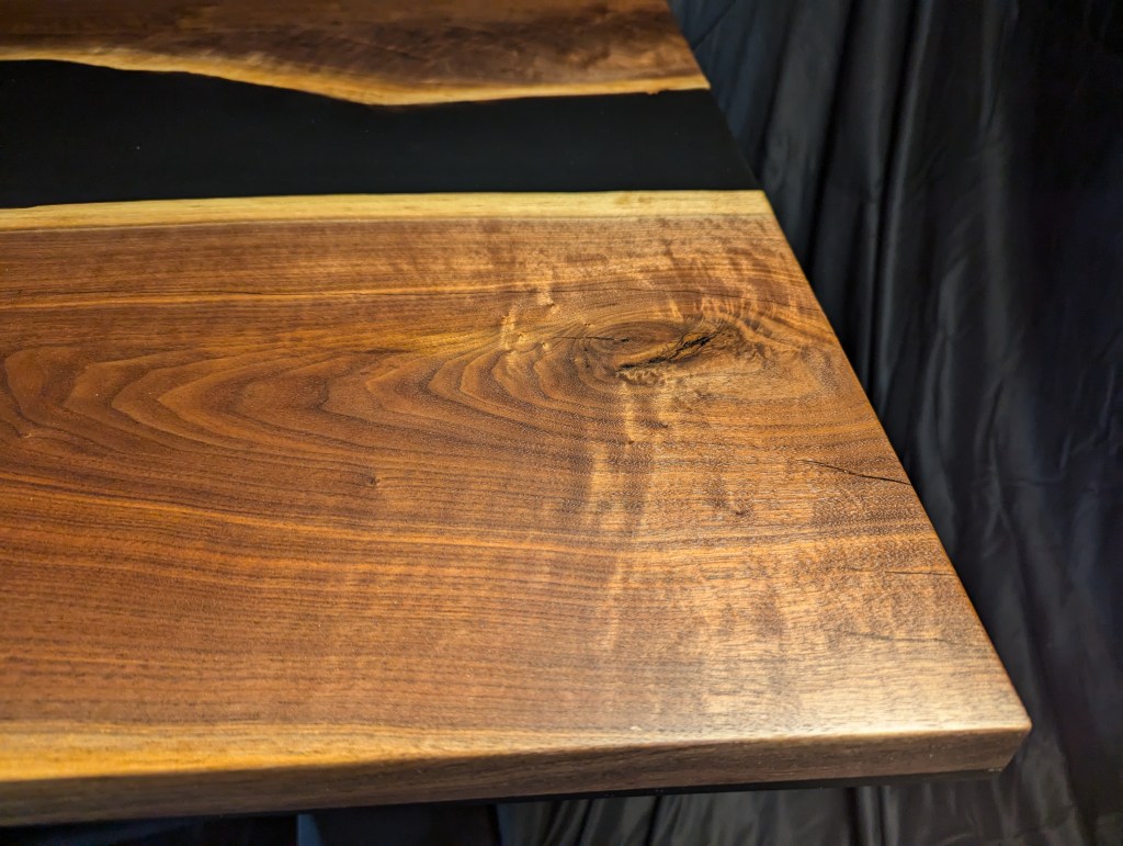 Close-up view of a handcrafted black walnut dining table showing the unique grain and live-edge detail of the wood surface.