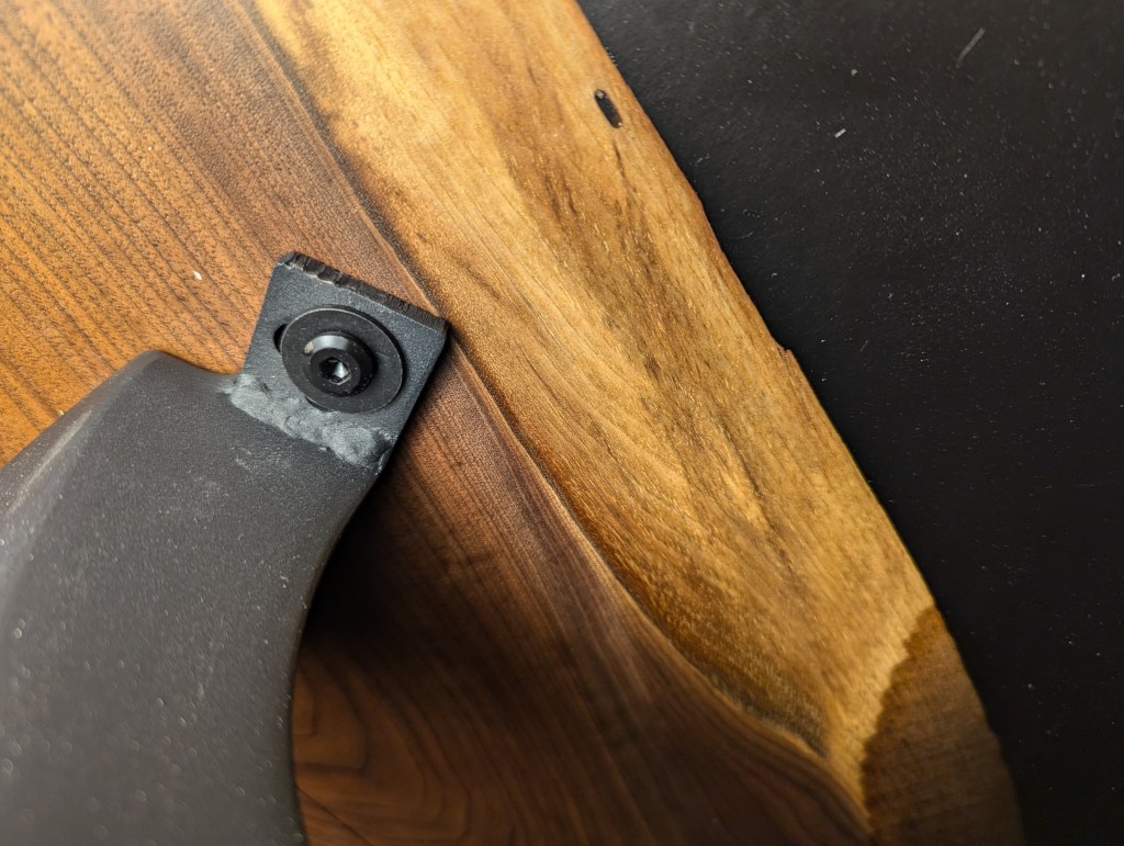 Close-up view of the connection between a black walnut tabletop and a polished steel leg, showcasing the natural grain of the wood and the sleek design of the leg.