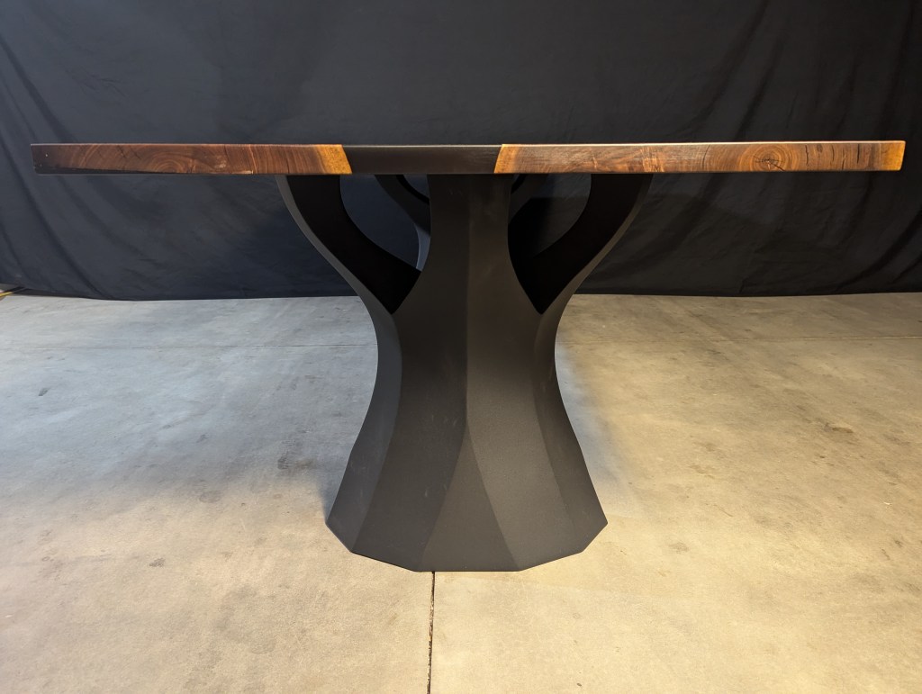 Side view of a handcrafted black walnut dining table featuring a unique live-edge design and modern black steel base.