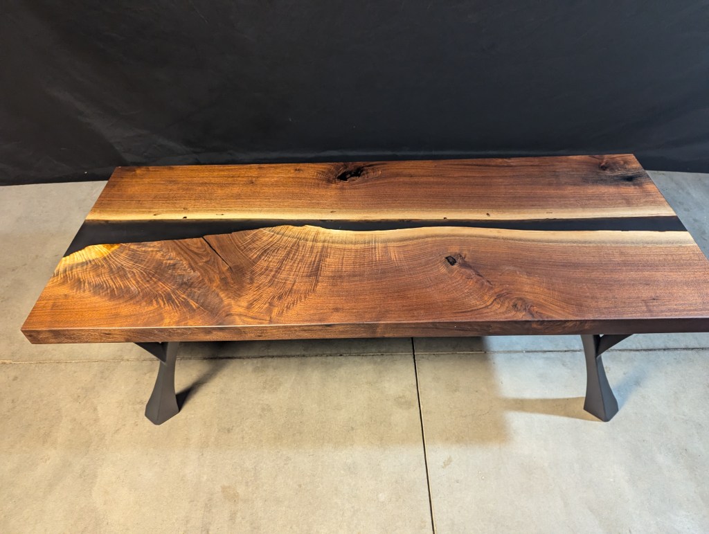 Top view of a handcrafted black walnut dining table featuring a live-edge design and modern polished steel legs.