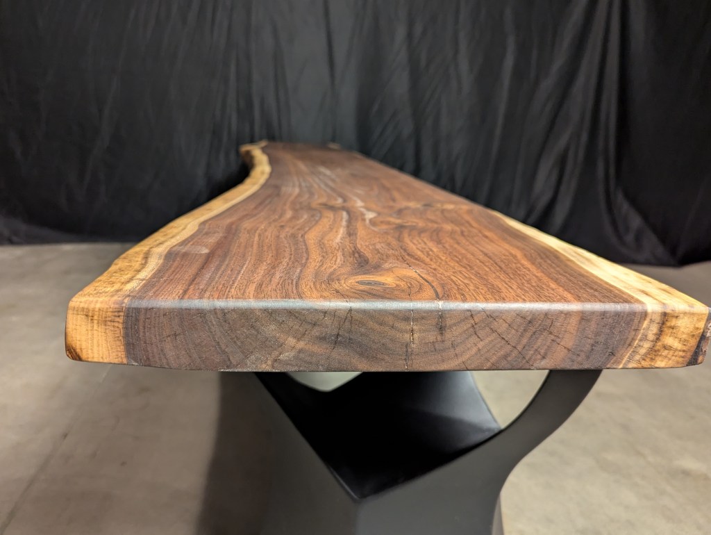 Close-up view of a beautifully crafted wooden tabletop with a natural edge, showcasing rich grain patterns and variations in color.