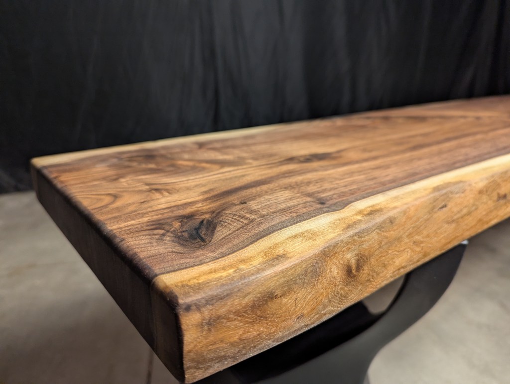 Close-up of a wooden table edge showcasing rich grain patterns and a smooth finish against a dark background.
