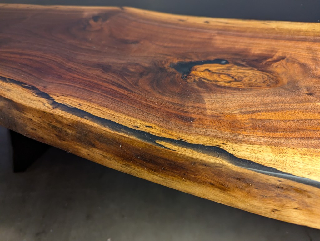 Close-up of a handcrafted black walnut table showcasing live edges and black epoxy resin fill.