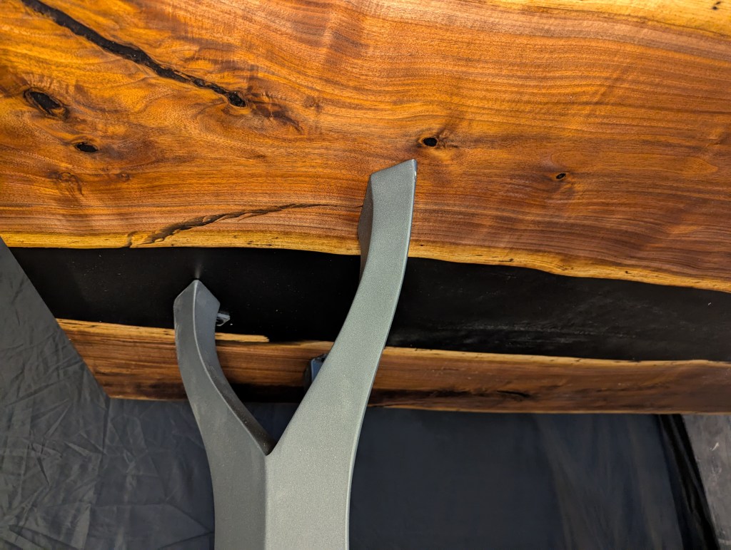 Close-up view of a handcrafted wooden table featuring a live edge black walnut slab and a brushed steel leg.