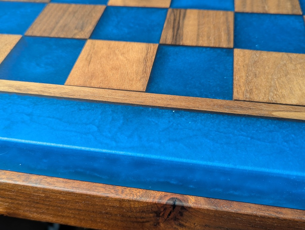 Close-up of a custom chess board featuring alternating light wood squares and a pacific blue epoxy resin surface.