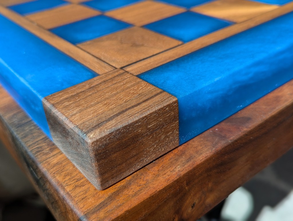 Close-up view of a custom chess board featuring dark walnut wood and pacific blue epoxy resin, highlighting the detailed craftsmanship and vibrant colors.