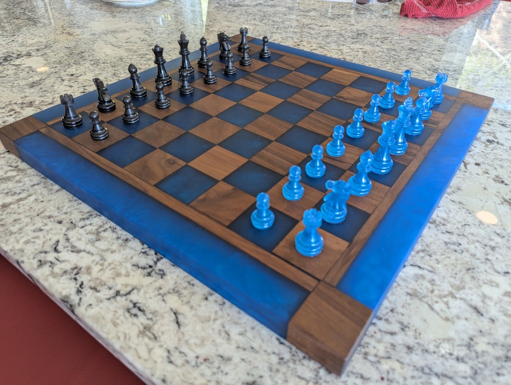 A custom chess board made from black walnut and dyed pacific blue epoxy resin, featuring matching blue chess pieces.