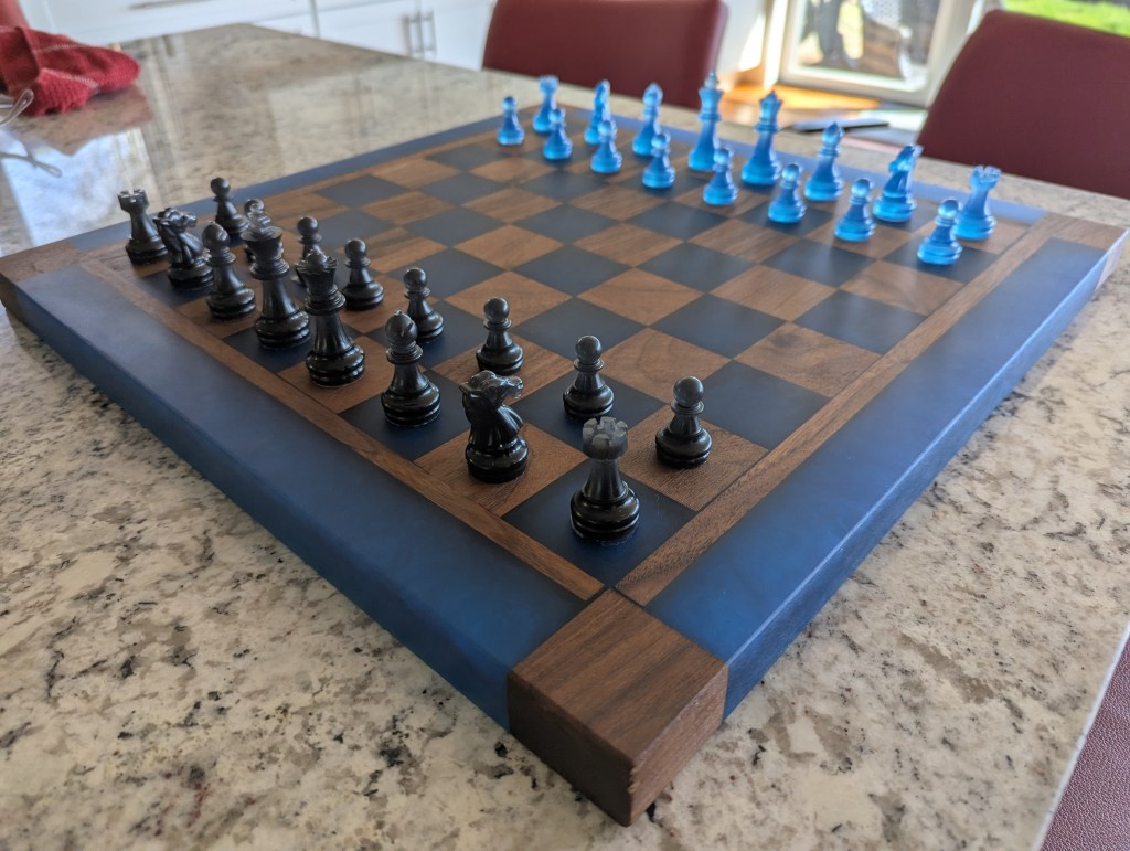 Custom chess board made from black walnut and dyed blue epoxy resin, featuring handmade chess pieces.