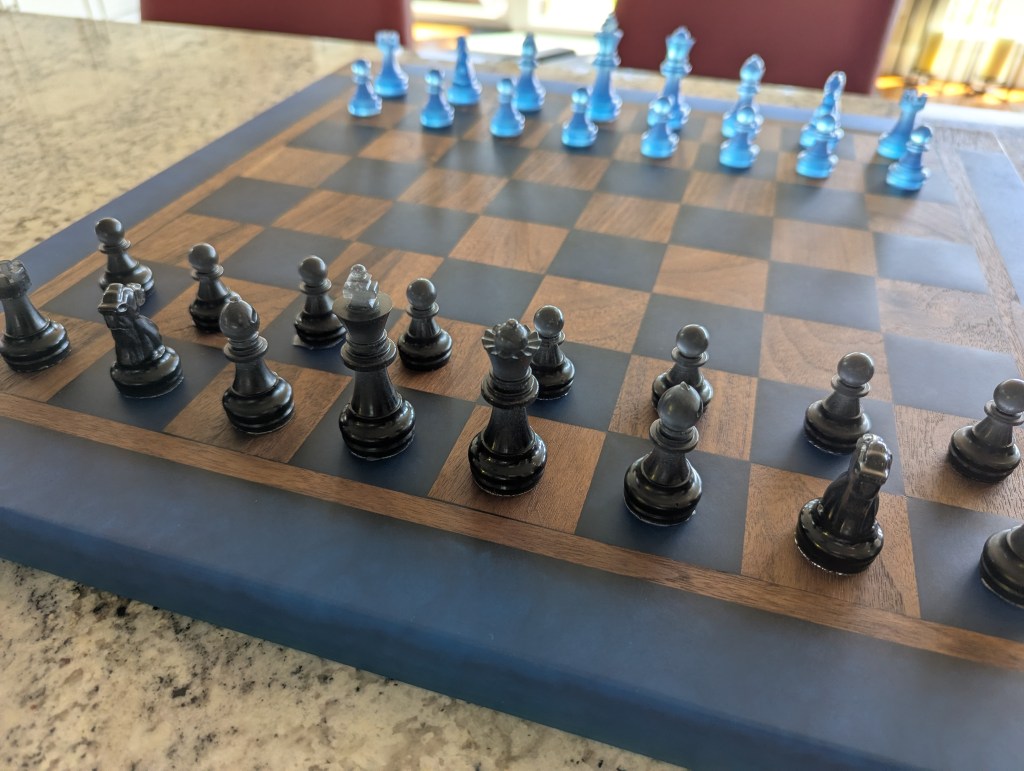 A close-up view of a custom chess board made from black walnut, featuring hand-crafted black and pacific blue chess pieces, with a checkered design.
