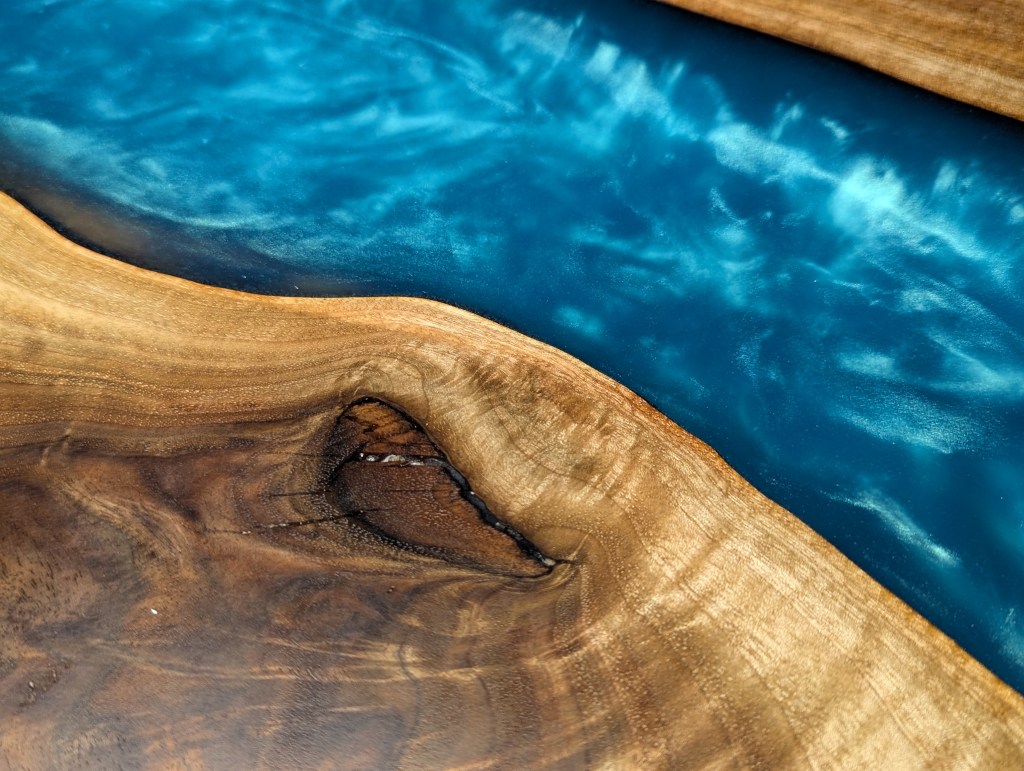 Close-up of a handcrafted black walnut river table featuring a vibrant Caribbean blue epoxy river between two wooden slabs.