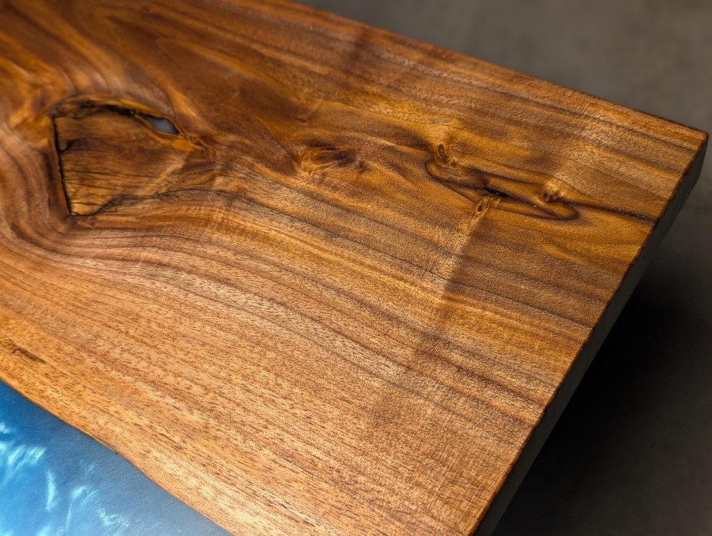 Close-up of a handcrafted black walnut river table featuring a vibrant blue epoxy river that mimics tropical water, highlighting the wood's grain and live edges.