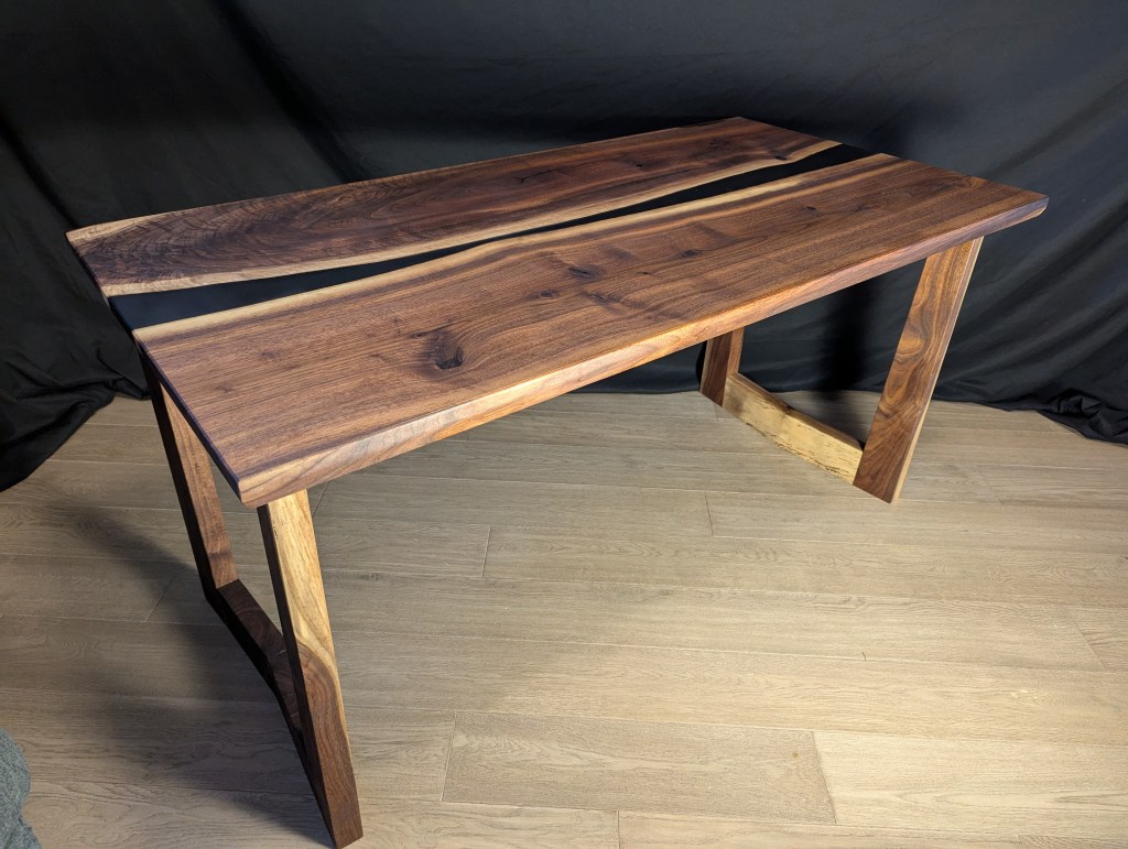 Handcrafted highline executive desk made of solid black walnut with a matte black epoxy river, featuring custom-cut angular legs and a live edge top.