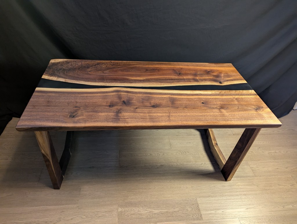 A handcrafted Highline Executive Desk made from solid black walnut with an epoxy river running through the middle. It features custom-cut angular legs and preserves the live edge of the wood.