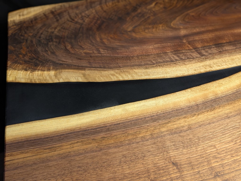 Close-up view of a handcrafted desk featuring a solid black walnut surface with a matte black epoxy river inlay.