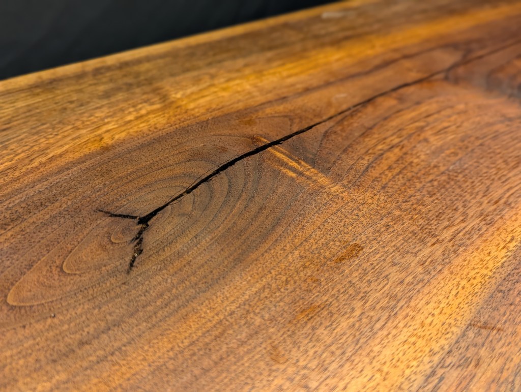 Close-up of a solid black walnut desk surface, showcasing a natural crack and intricate grain patterns.