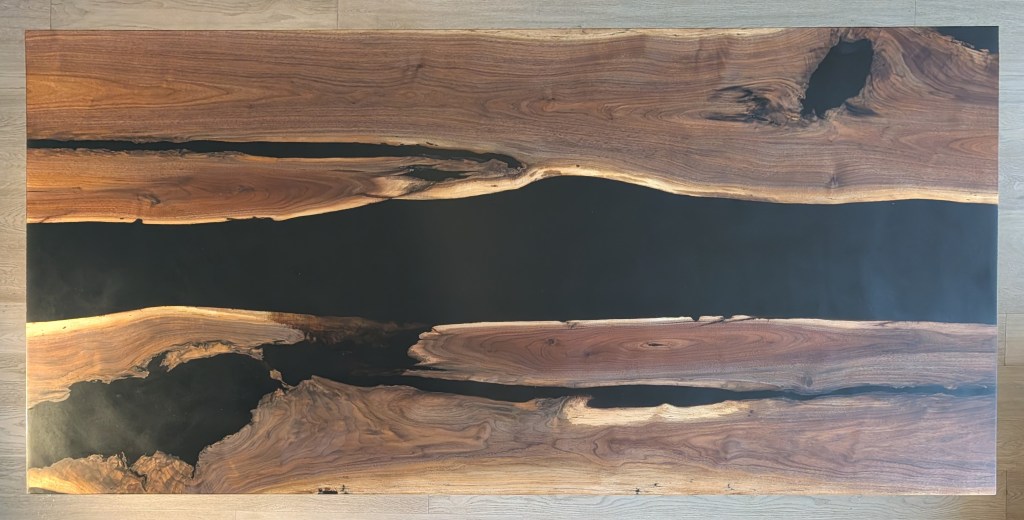Top view of an adjacent-slab black walnut dining table with a black epoxy river.